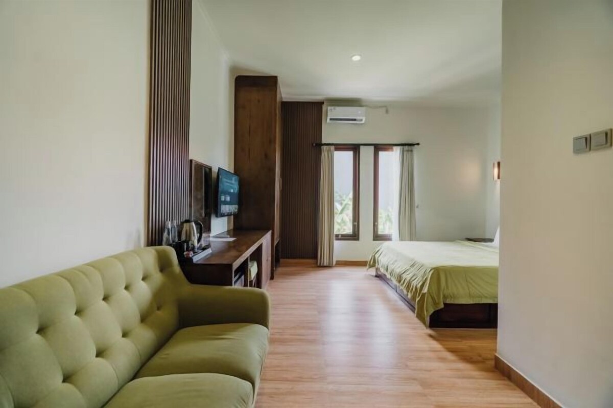 A hotel room with a sofa, a TV, a bed, and a window with curtains.