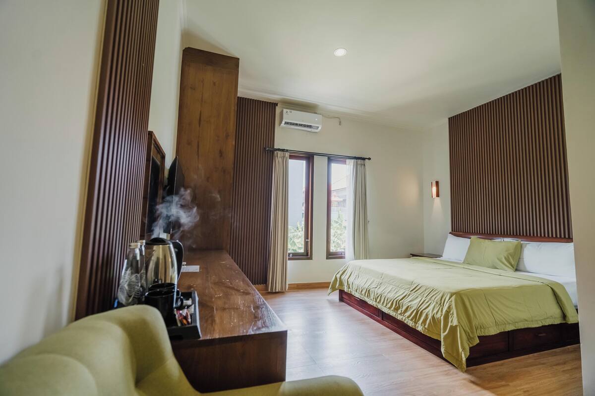 A modern bedroom with a large bed, a wooden bench, and a view of the outdoors through the window.