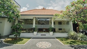 A modern building with a tiled roof, a covered entrance, and potted plants. - You Suite Seminyak (Legian)