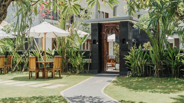 A pathway leading to a building with a stone entrance, surrounded by lush greenery and outdoor seating areas. - You Suite Seminyak (Legian)