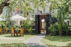 A pathway leading to a building with a stone entrance, surrounded by lush greenery and outdoor seating areas. - You Suite Seminyak (Legian)