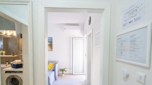 A hallway with a washing machine, a sink, a mirror, a plant, and a couch.