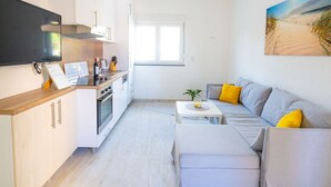 A modern, compact living space with a kitchenette, a sofa with yellow cushions, and a beach-themed painting on the wall.