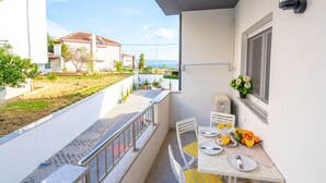 A balcony with a dining table set for two, a small garden area, and a view of neighboring houses.