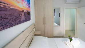 A bedroom with a bed, a wooden wardrobe, a wall-mounted air conditioner, and a painting of a beach scene. - Lucius 1 by Interhome (Podstrana)
