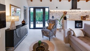 Una sala de estar moderna con techo de madera, un sillón estampado de cebra, sofá color beige, mueble de TV negro y pared de piedra.