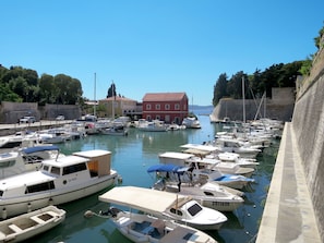 Boats docked at the marina, adjacent to a stone wall and a red building with a tiled roof.