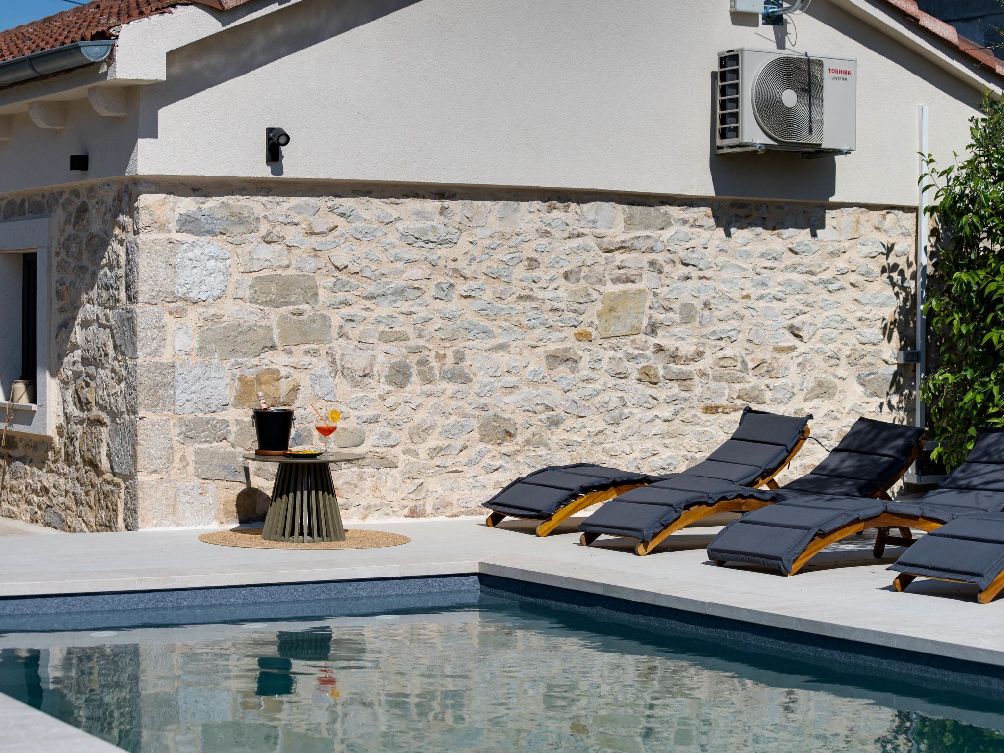 Area piscina con pareti in pietra, fontana decorativa e poltrone relax.