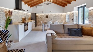 Un interior acogedor con pared de piedra, vigas de madera en el techo, una zona de comedor y un sofá con cojines.