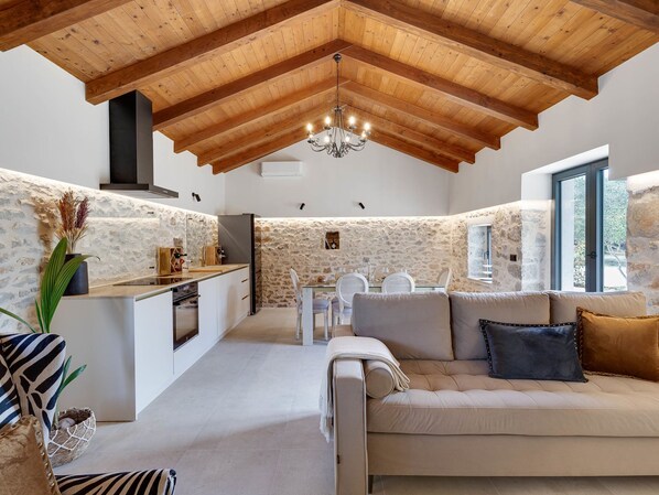 A cozy interior with a stone wall, wooden ceiling beams, a dining area, and a sofa with cushions.