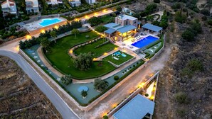 An aerial view of a residential property with a swimming pool, landscaped gardens, and a well-lit outdoor area. - Epitome Villa Aegina (Aegina)