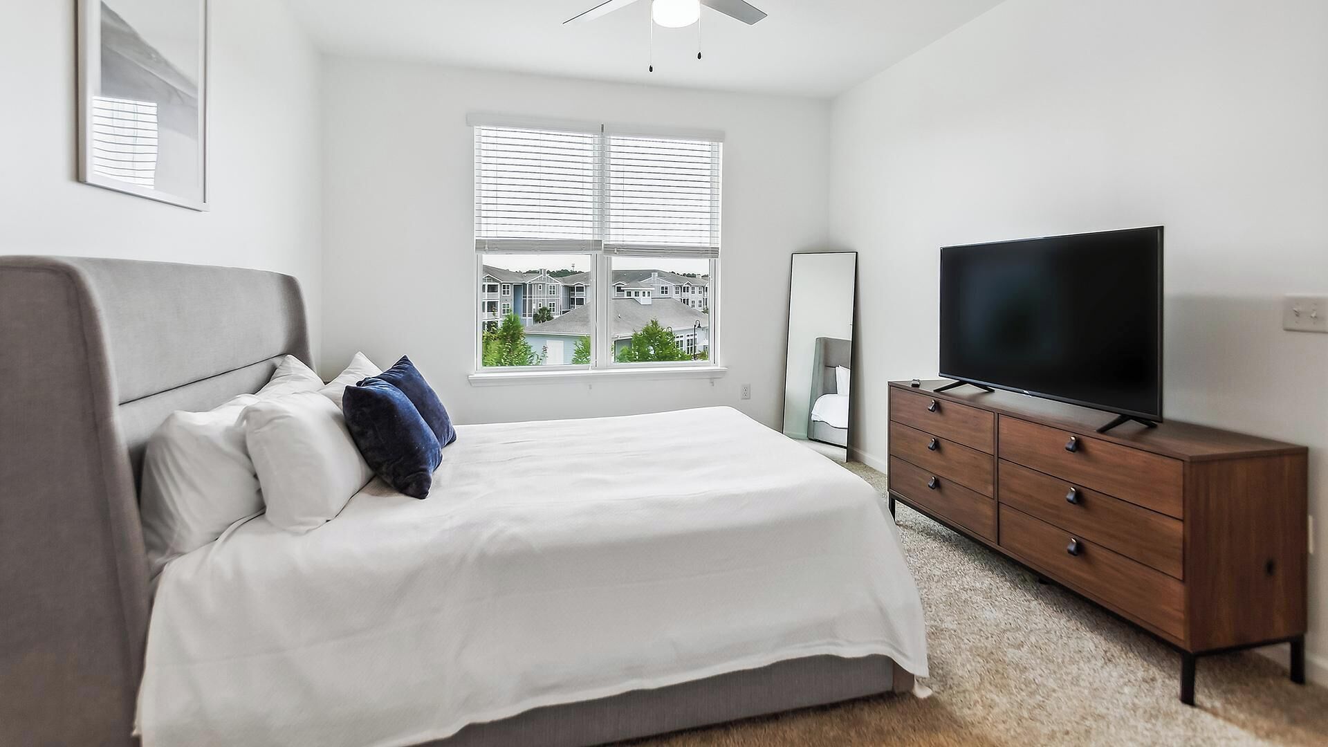A bedroom with a bed, a dresser, a TV, and a window with blinds.
