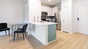 Une cuisine compacte avec des meubles blancs, un îlot central et un coin repas comprenant une table et des chaises en verre.