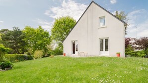 Ein modernes, zweistöckiges Haus mit weißer Fassade, einer Haustür und einer kleinen Veranda mit Sitzgelegenheit.