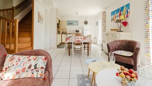 Ein gemütliches Wohnzimmer mit einer Couch, einem Esstisch mit Stühlen, einer Küche im Hintergrund und einer Treppe.