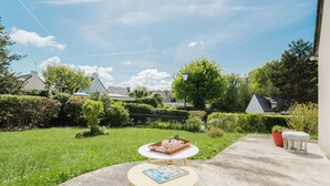 Eine Terrasse mit rundem Tisch und Stühlen, ein kleiner Garten und eine Aussicht auf Häuser im Hintergrund.