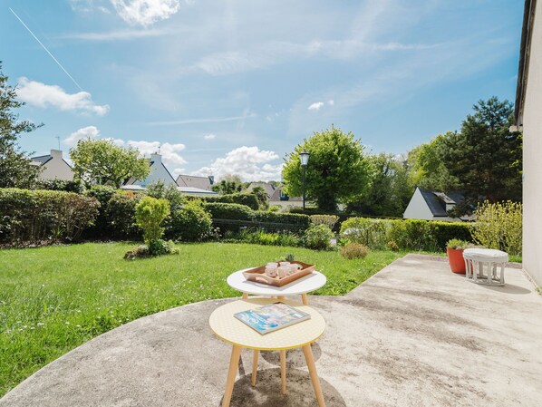 A patio with a round table and chairs, a small garden, and a view of houses in the background.