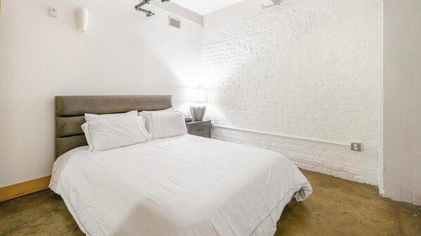 A bedroom with a bed, nightstand, and a white brick wall.