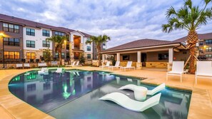 A swimming pool with lounge chairs and a covered area, surrounded by multi-story buildings with stone facades. - Landing | Stunning 1BD, Gym, Clubhouse (Pflugerville)