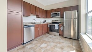 Una cocina moderna con electrodomésticos de acero inoxidable, encimeras de granito y muebles de color marrón.