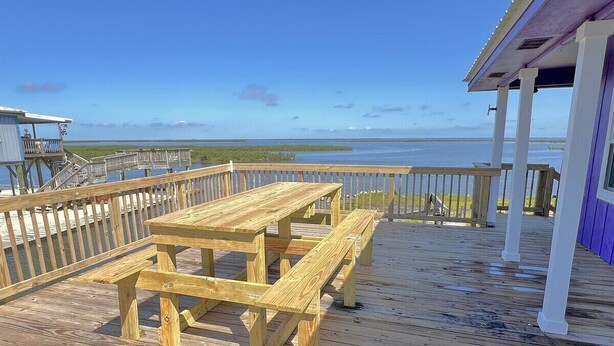 A wooden deck with a picnic table and benches, overlooking a body of water.