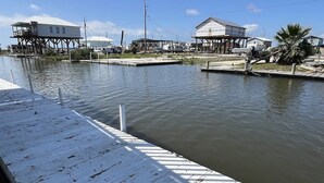 A waterfront property with a wooden dock extending into calm water, surrounded by residential buildings and a palm tree.