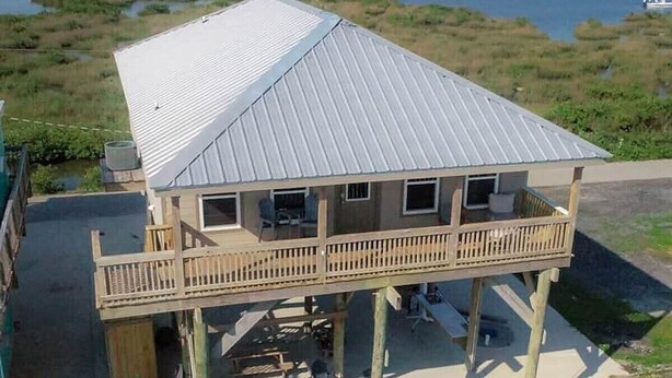 Een twee verdiepingen tellend huis met een balkon, een metalen dak en uitzicht op een waterpartij.
