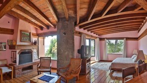 A cozy room with a fireplace, wooden furniture, and large windows offering a view of the outdoors.