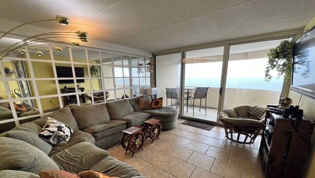 A spacious living area with a large sofa, a coffee table, and a TV. There is a balcony with a view of the ocean. - Oceanfront 3BR , Pool, 2 Balconies, Views by Karsons Keys (Ocean City)