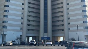 A tall, modern building with a central elevator shaft, multiple floors, and a parking lot with cars. - Oceanfront 3BR , Pool, 2 Balconies, Views by Karsons Keys (Ocean City)