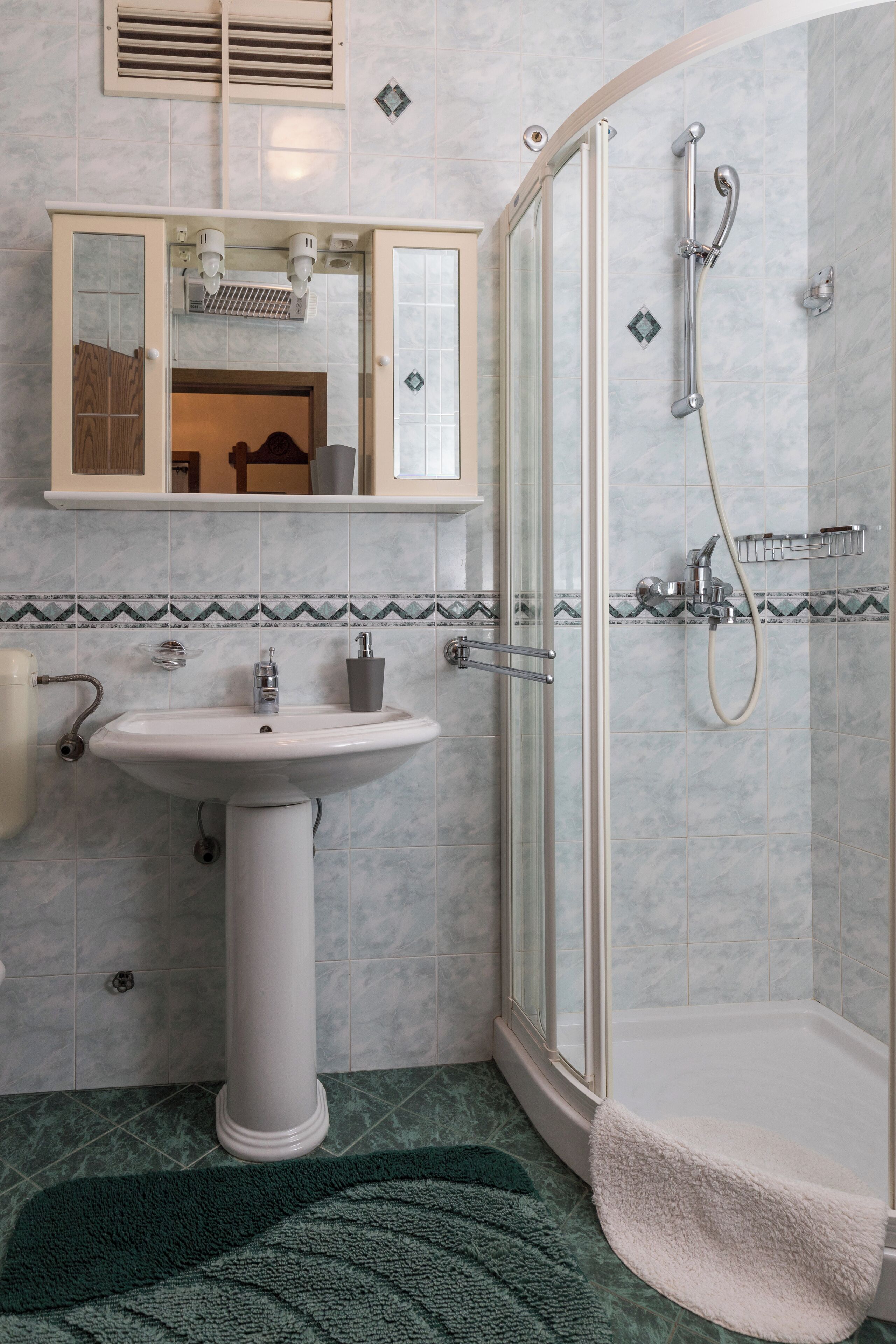 A bathroom with a pedestal sink, a glass-enclosed shower, and a mirror above the sink.