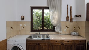 A kitchen with a washing machine, a sink, wooden cabinets, a window with a curtain, and a radio. - Apartment Vukic (Dubrovnik)