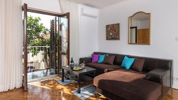 A modern living room with a sofa, a coffee table, and a dining table. There is a sliding glass door leading to an outdoor area. - Apartment Vukic (Dubrovnik)