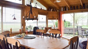 Ein Essbereich mit Holztisch und -stühlen, einer hängenden Leuchte und Blick auf einen See durch große Fenster.