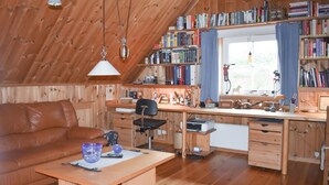 Ein gemütliches Wohnzimmer mit Holzboden, einem Ledersofa, einem Holztisch und einem Bücherregal voller Bücher.