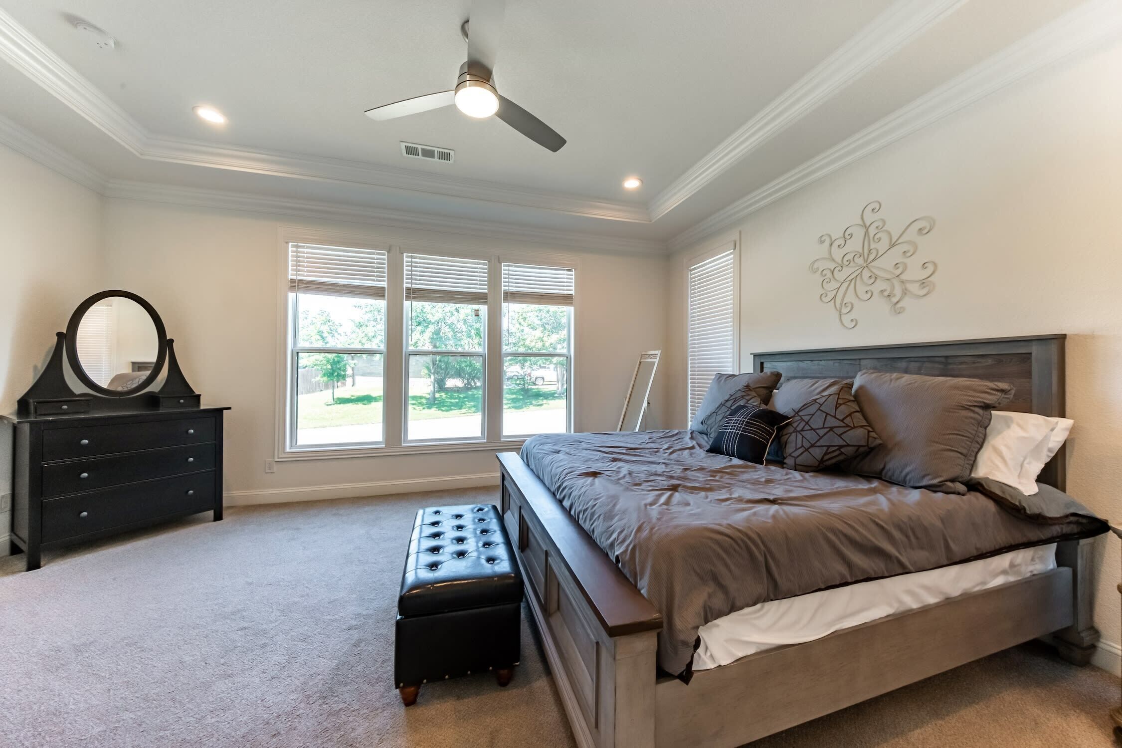 A bedroom with a bed, dresser, bench, and a ceiling fan.