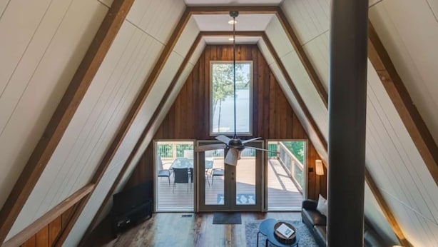 Una habitación con techos altos, interiores de madera, un ventilador de techo y vistas a una terraza exterior.