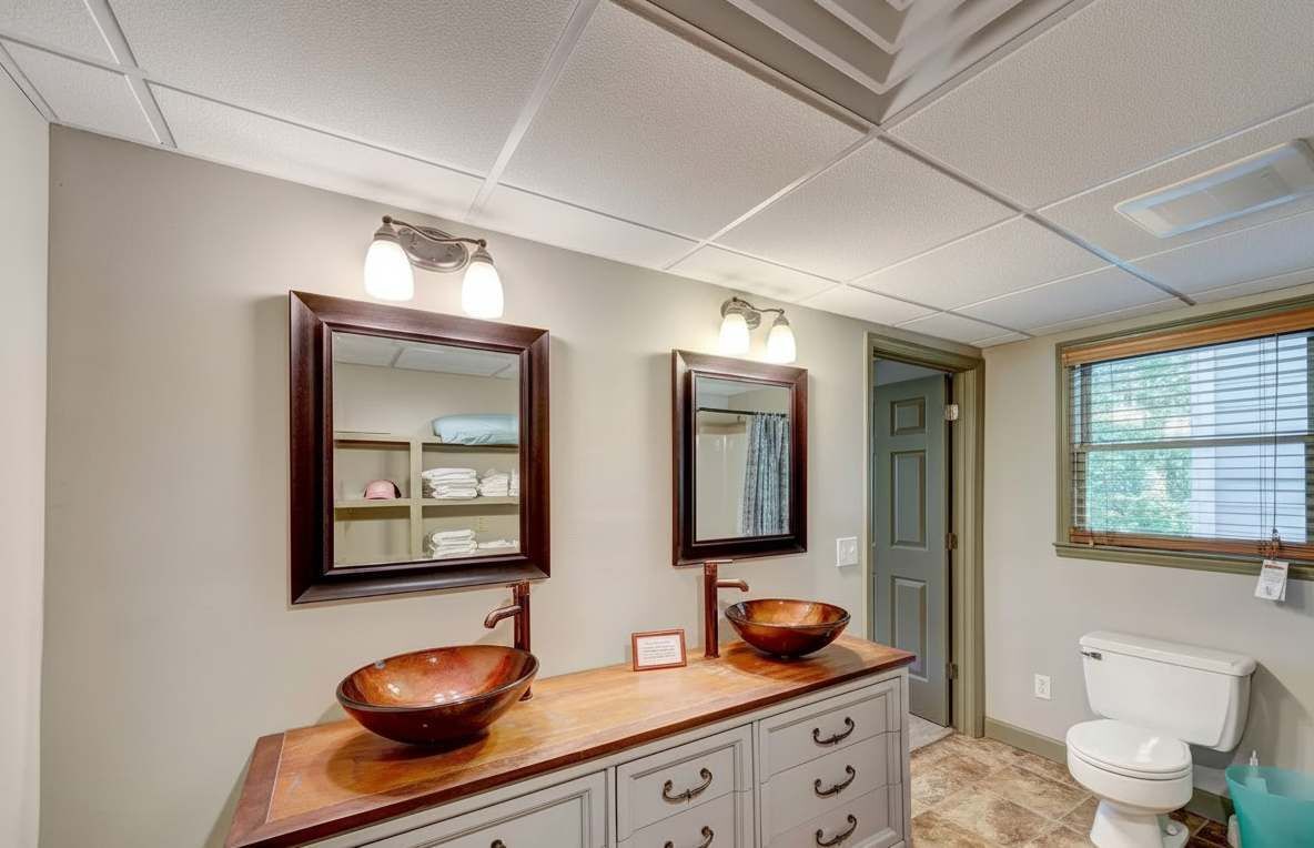 Un baño con dos espejos, un lavabo con un recipiente grande y un inodoro.