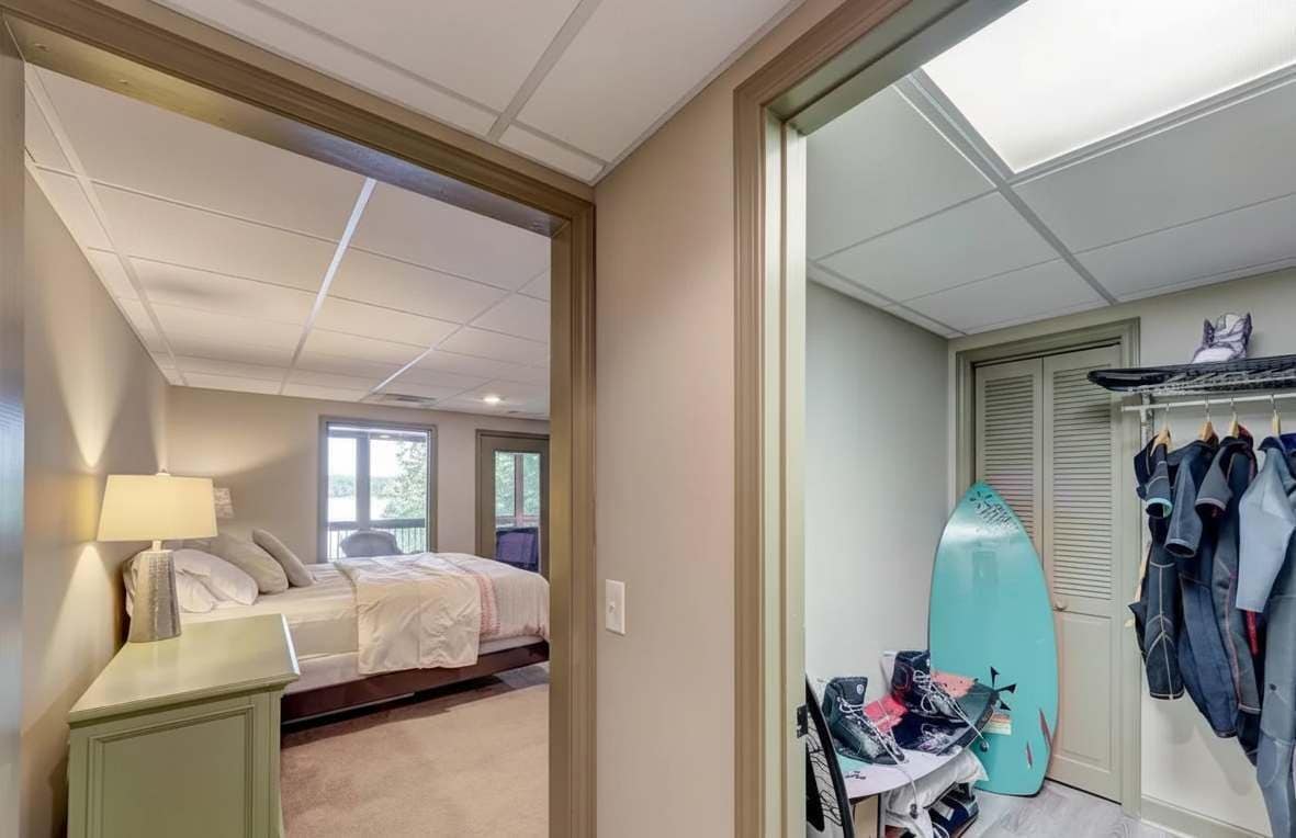 A bedroom with a bed, a nightstand, a surfboard, and a closet with hanging clothes.