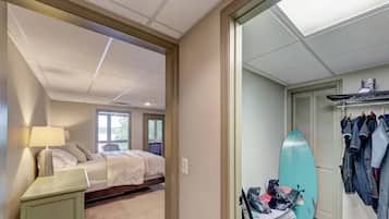 A bedroom with a bed, a nightstand, a surfboard, and a closet with hanging clothes.