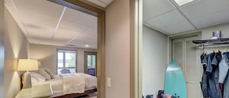 A bedroom with a bed, a nightstand, a surfboard, and a closet with hanging clothes.