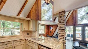 A spacious kitchen with granite countertops, wooden cabinets, and a stone accent wall. - Cozy 3BR Cabin with Lake View in Dawsonville (Dawsonville)
