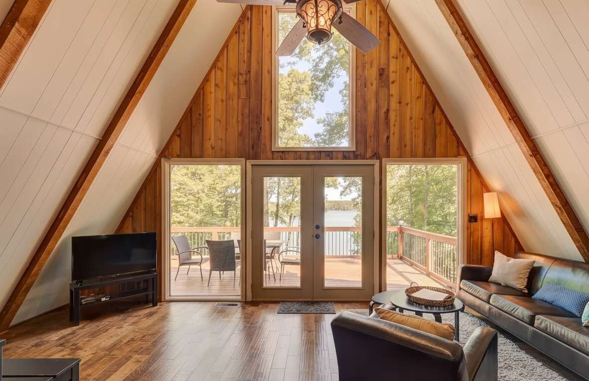A cozy attic bedroom with a large sliding glass door leading to a balcony, a ceiling fan, and a TV on a stand.