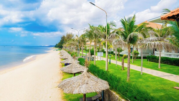 A beach resort with a sandy shoreline, palm trees, and thatched umbrellas. - Blooming Lotus Resort (Tien Thanh)
