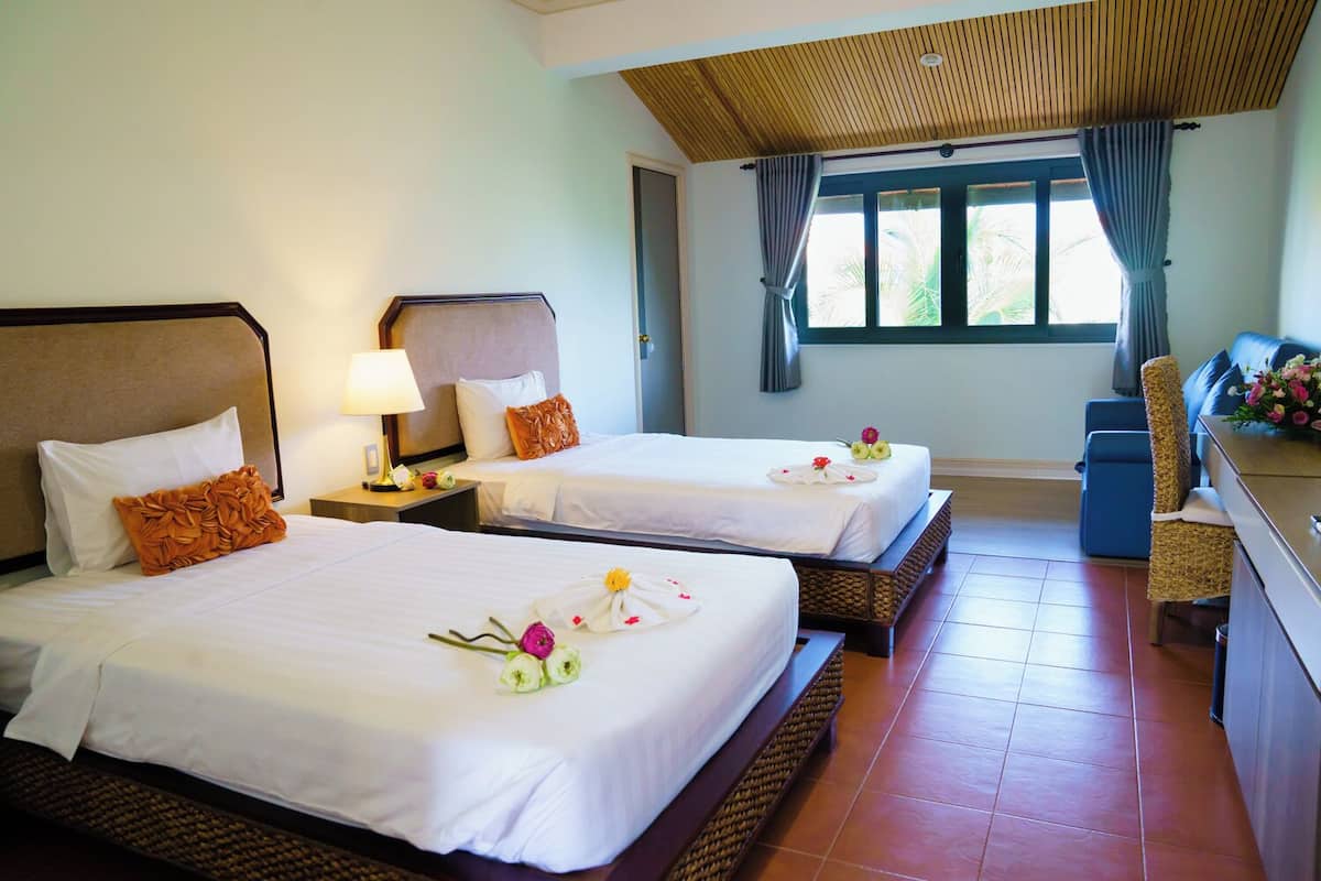 A hotel room with two beds, a desk, a chair, and a window with curtains.
