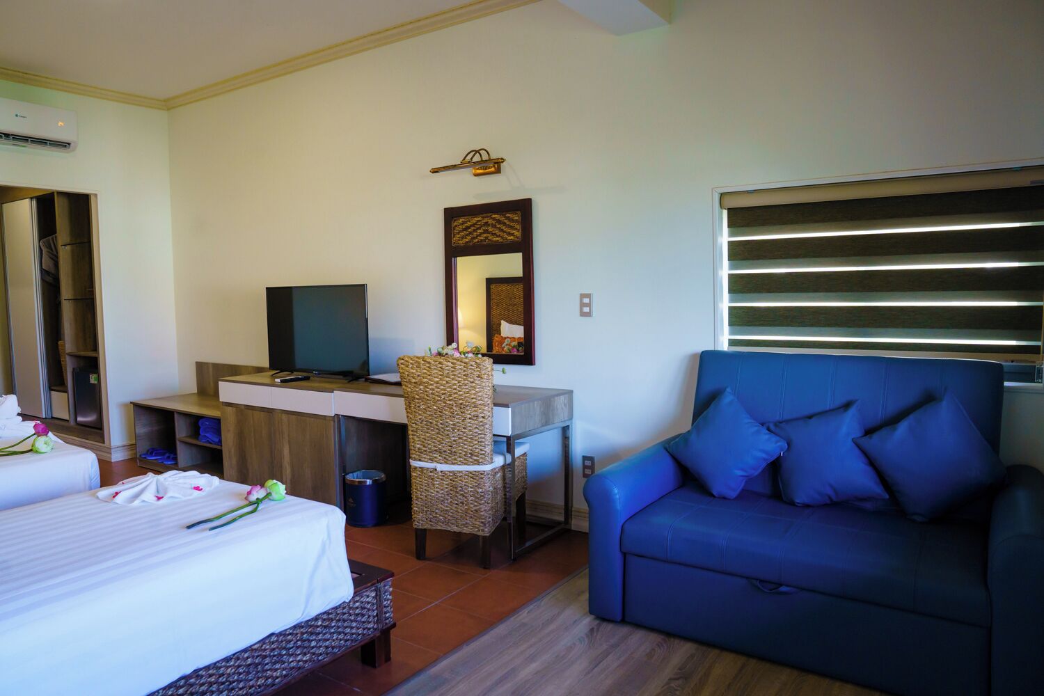 Una habitación de hotel con una cama, un escritorio con computadora, un sofá azul y un espejo.