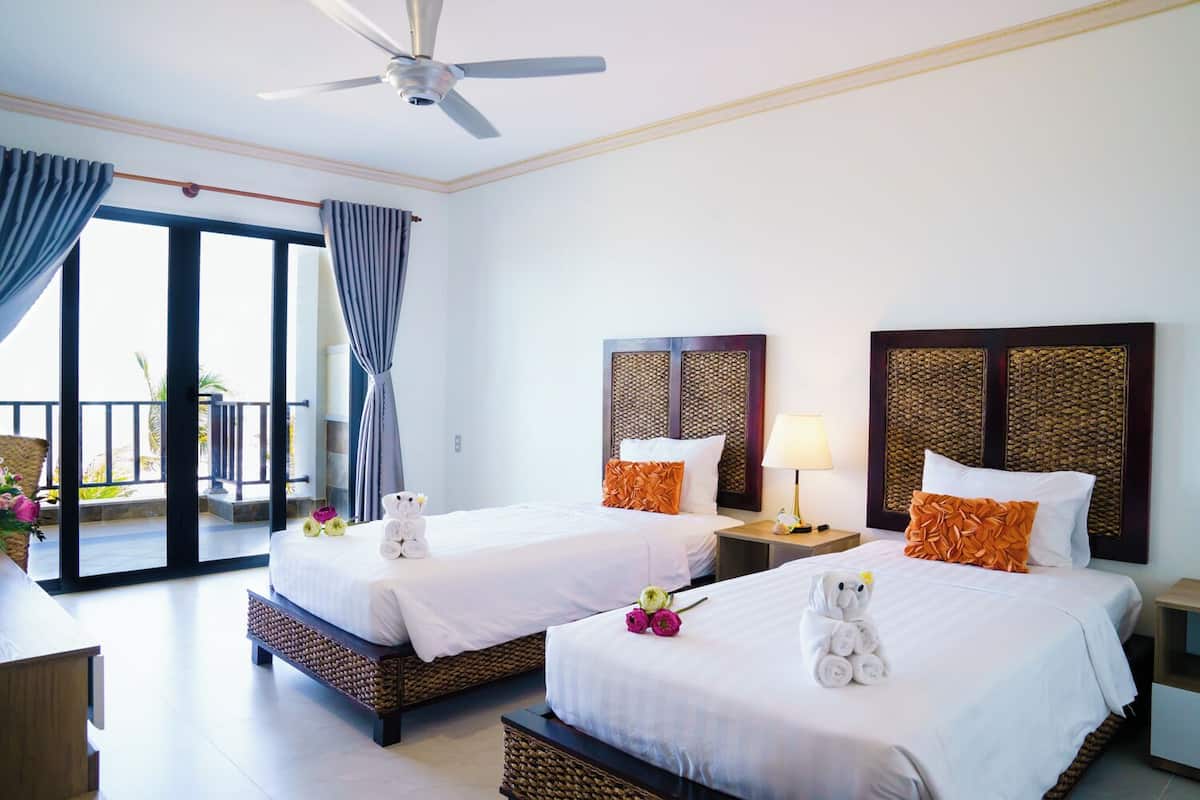 A hotel room with two beds, a balcony, and a ceiling fan.