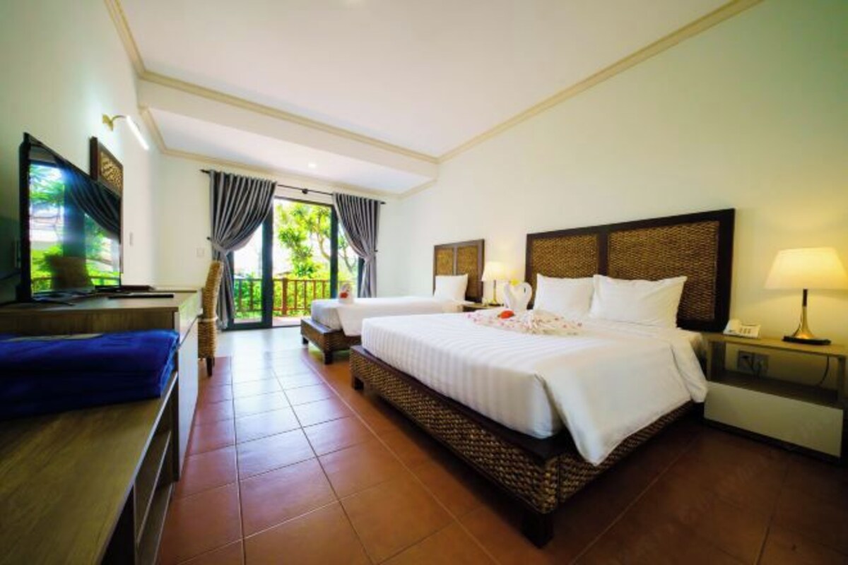 A hotel room with a large bed, two bedside tables, a TV, and a balcony with curtains.
