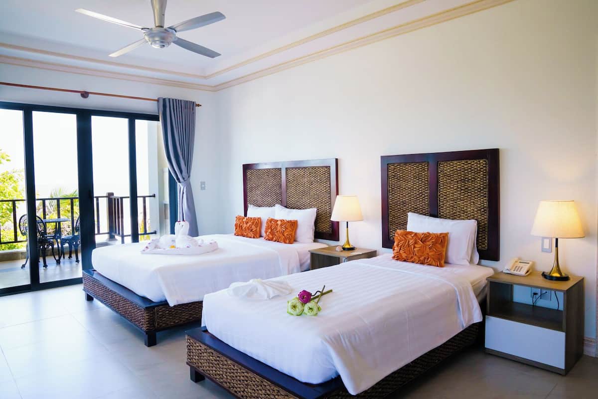 A hotel room with two beds, a balcony, and a view of the outdoors.