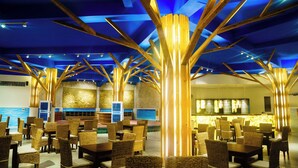 A spacious indoor area with wicker furniture arranged in rows, a bar area with a counter, and a ceiling with geometric wooden structures. - Blooming Lotus Resort (Tien Thanh)